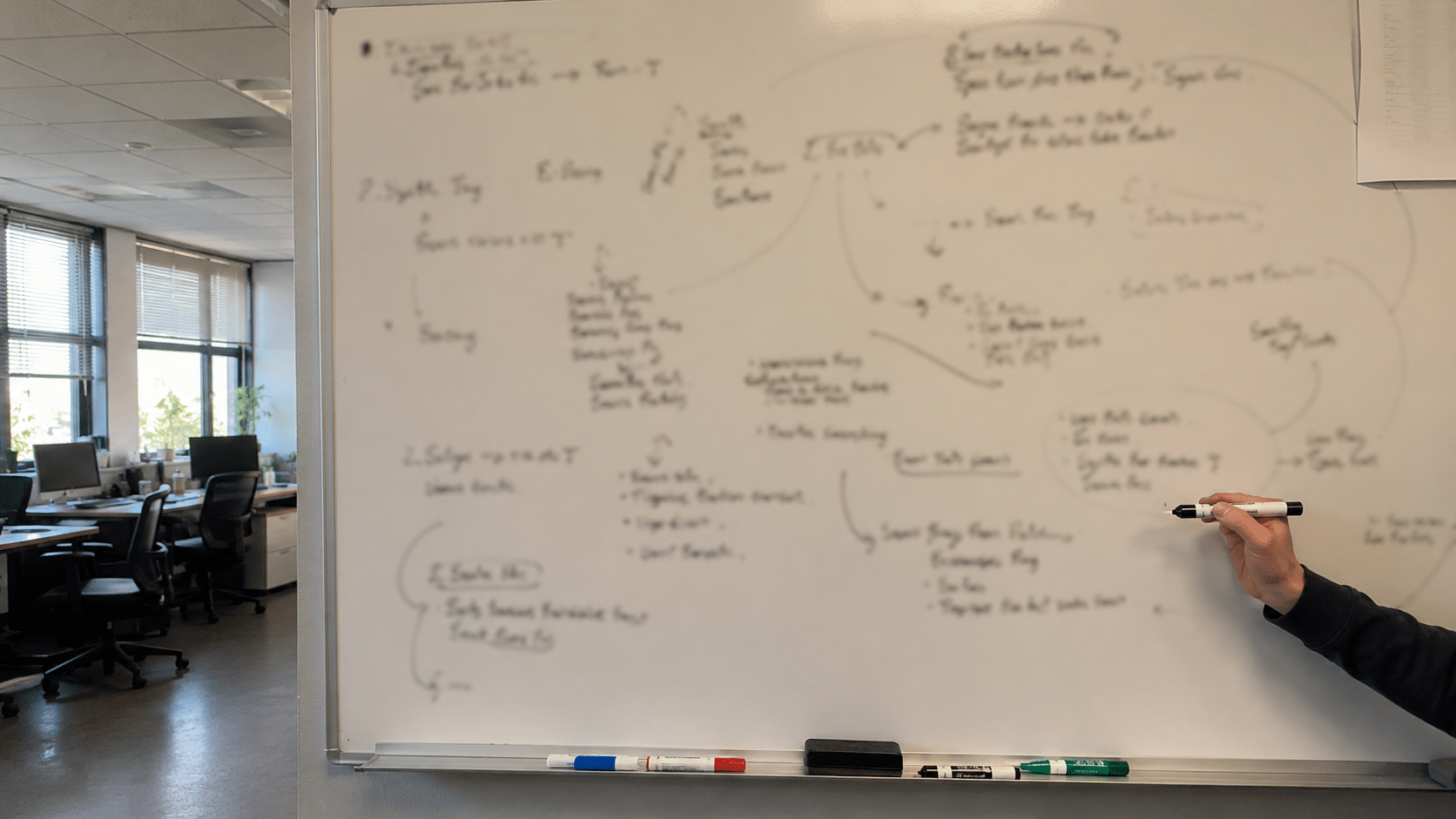 A small-business back-office whiteboard covered in handwritten planning notes with illegible text, a hand holding a dry-erase marker (no faces, no logos)