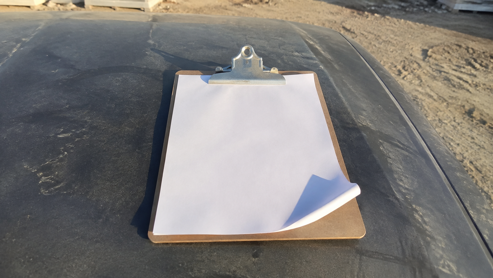 A single printed page on a clipboard resting on a truck hood at a construction staging area