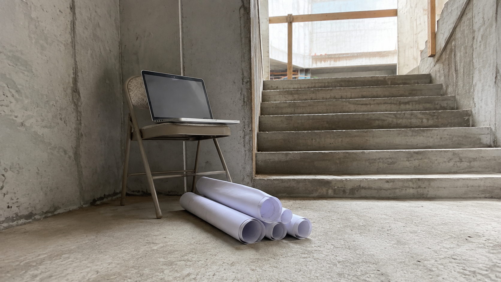 A laptop and rolled drawings in a concrete stairwell of a building under construction