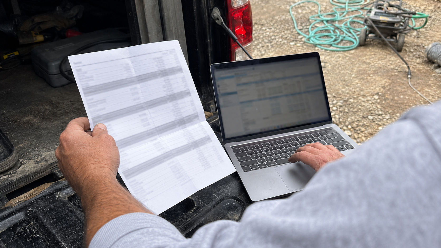 A contractor comparing a printed estimate against a laptop on a truck tailgate at a job site