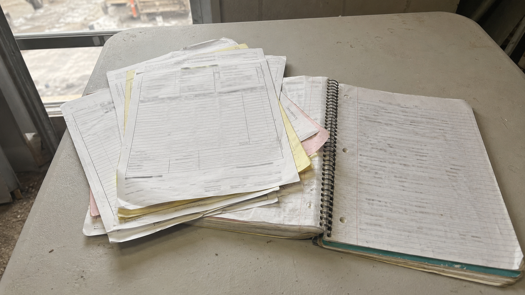 Material delivery tickets and a notebook on a folding table inside a job site trailer