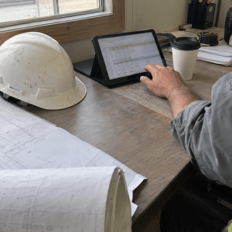 Construction project manager reviewing a job cost report on a tablet at a jobsite trailer