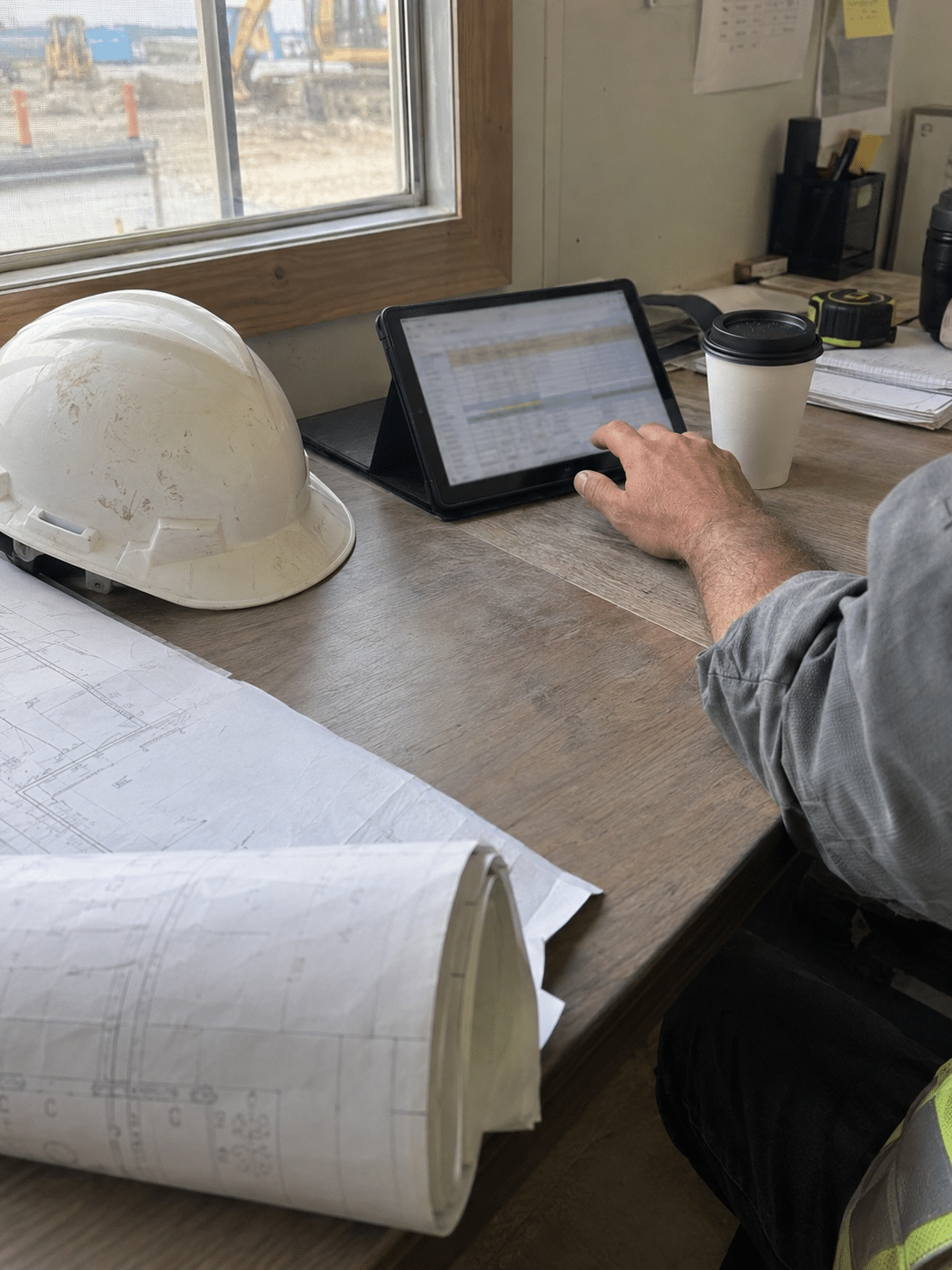 Construction project manager reviewing a job cost report on a tablet at a jobsite trailer