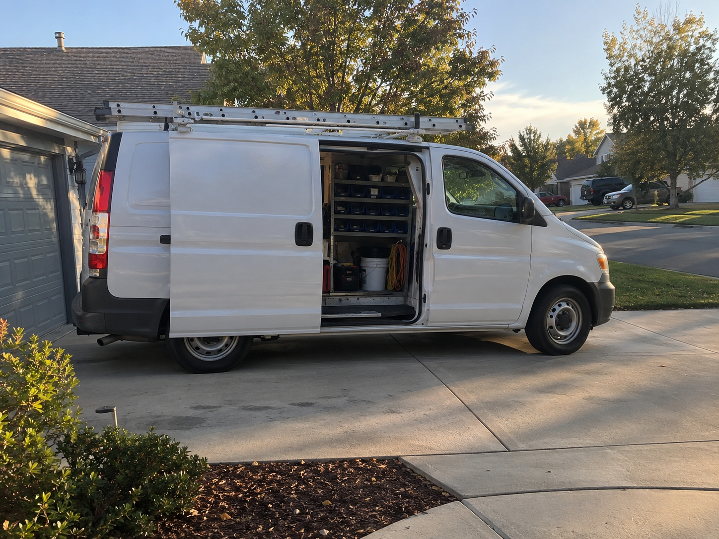 Service technician van parked outside a job with the side door open showing organized parts bins